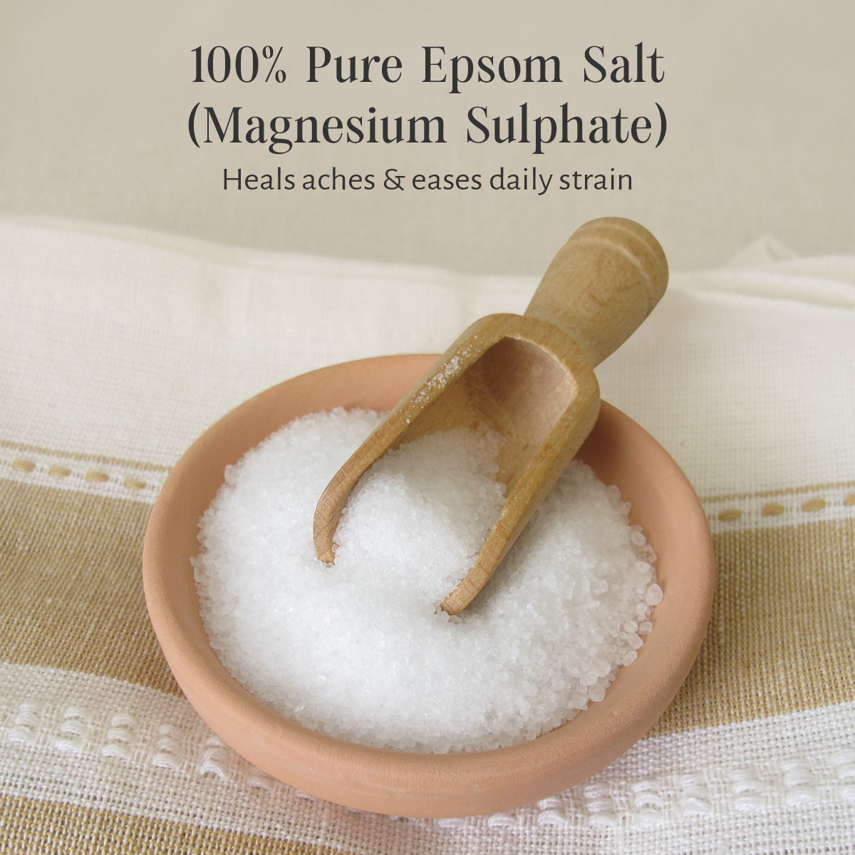Bowl of 100% pure Epsom salt with a wooden scoop on a textured fabric background.