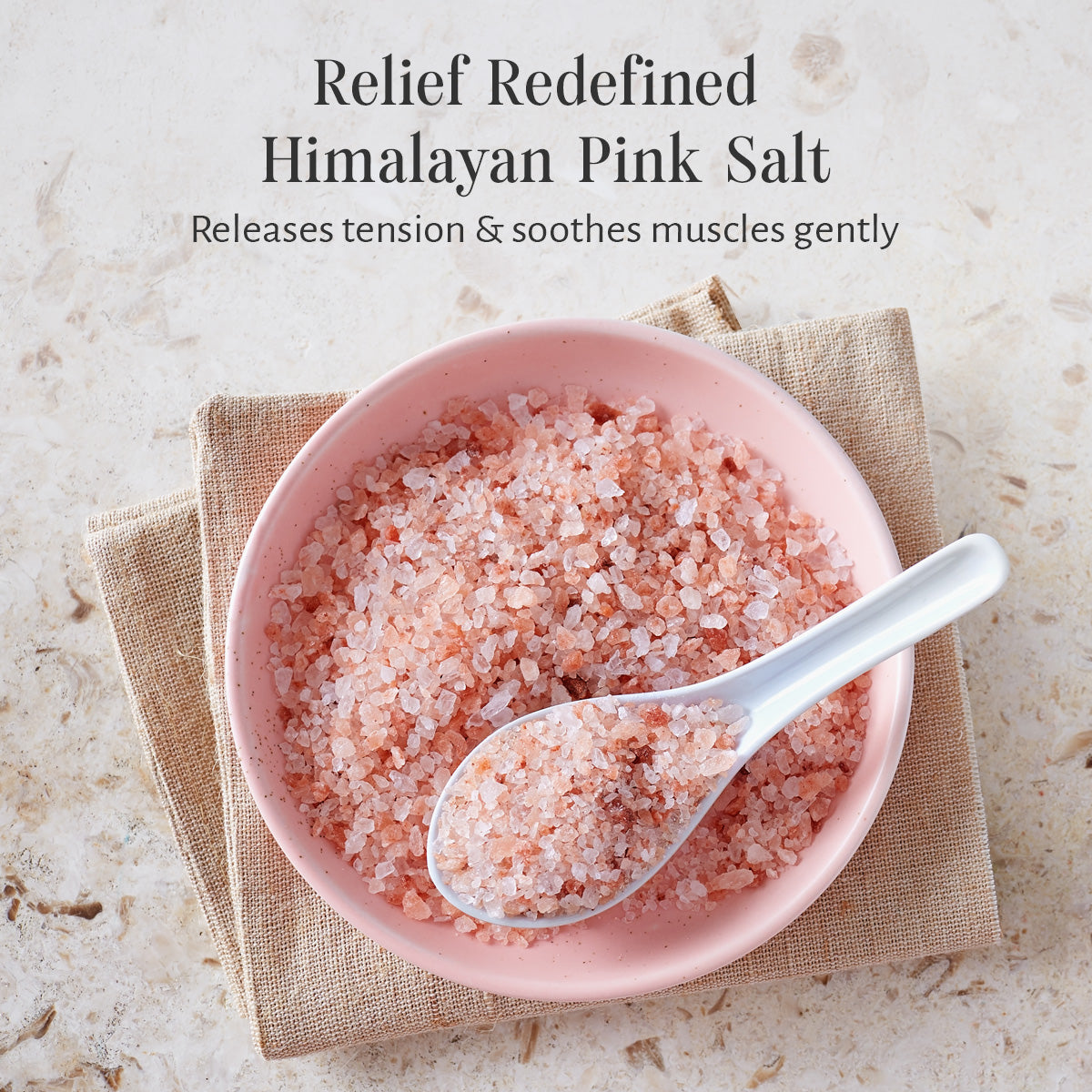 Pink bowl of Himalayan pink salt with a spoon on a textured surface, text about salt benefits.